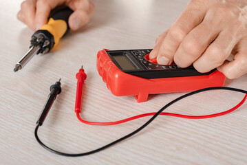 Closeup photo of screwdriver and multimeter in hands of male electrician