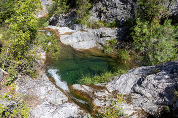 Small mountain lake with green transparent water and waterfall 