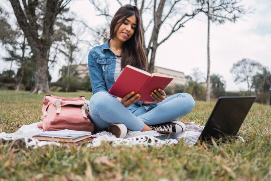 Student with book and laptop in park