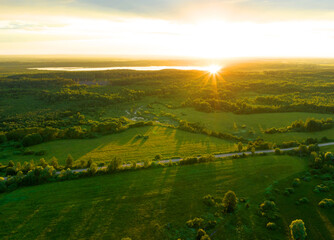 Fototapeta premium Lake at sunset in forest. Forest lake in wild at sunrise. Drone view of wetland in green colors. Road in Rural at field and forest. Clean air and ecology. Pond. Rural landscape and countryside.
