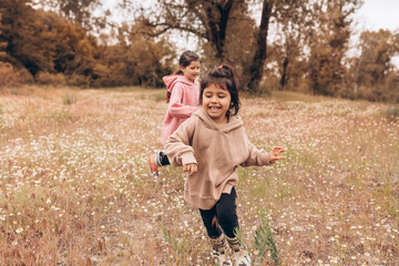 Two little girls in rubber boots and sweatshirts run and have fun against the background of the autumn forest