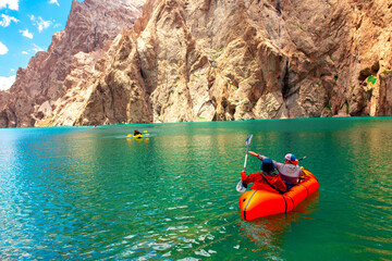 Kayaking on a mountain lake. Two men are sailing on a red canoe along the lake along the rocks. The theme of water sports and summer holidays.