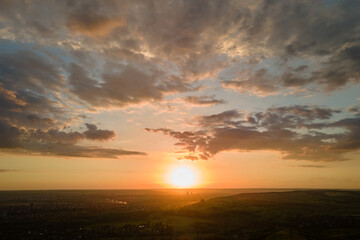 Bright colorful sunset sky with setting sun and vibrant clouds over dark landscape