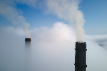 Coal power plant high pipes emitting black poisonous smoke moving upwards over white fog polluting air. Production of electrical energy with fossil fuel concept