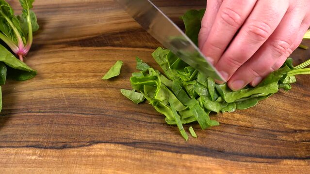 The cook cuts spinach leaves on a wooden cutting board.