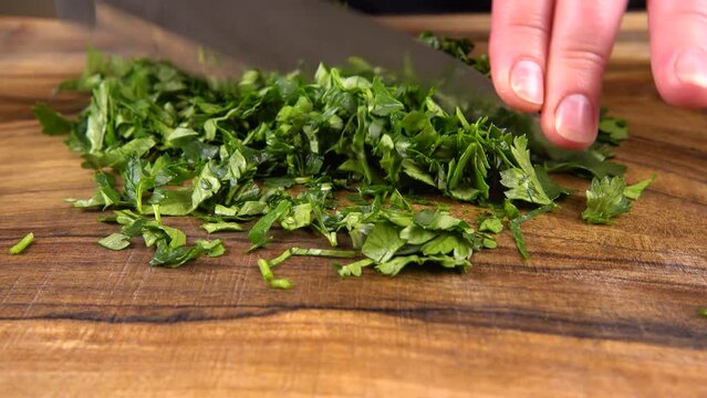 The cook cuts parsley on a wooden cutting board.