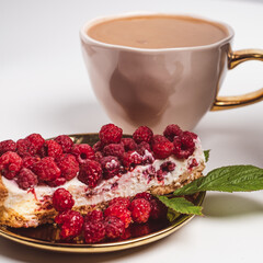 Delicious piece of cake with fresh raspberries and luxurious cup of coffee in background. White table. White background. Sweet concept. Excellent image for dessert banners. 