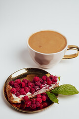 Delicious piece of cake with fresh raspberries and luxurious cup of coffee in background. Light grey background. Sweet concept. Excellent image for dessert banners. Place for your text.