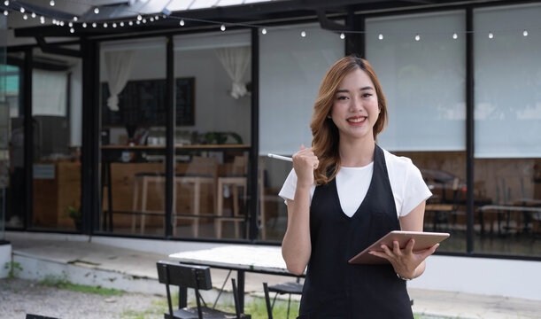 Attractive beautiful young Asian female restaurant or coffee shop waitress noting a customer's order on a digital tablet.