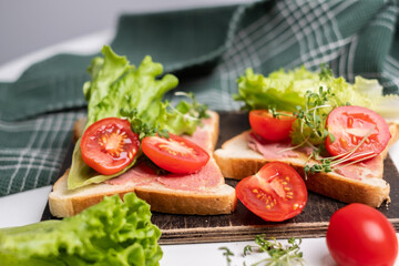 Close-up of delicious toasts decorated with microgreens and tomatoes and fresh lettuce. Healthy breakfast. Grey towel in background. White background.