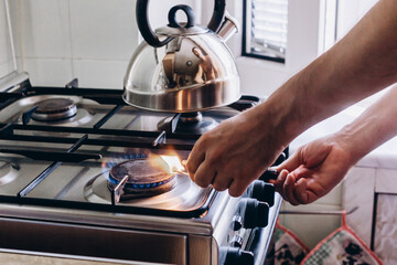 A man's hand with a match lights a gas burner or a gas stove in the kitchen - obrazy, fototapety, plakaty