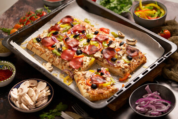 A piece of square pizza with basil pepperoni tomatoes and mushrooms on a iron tray