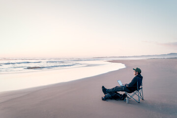 digital nomad sitting with laptop on the shore of the beach alone working relaxed and calm