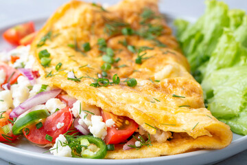 Homemade stuffed omelet on a plate. Egg omelet stuffed with fresh tomatoes, cheese and green parsley. Healthy vegetarian breakfast recipe.