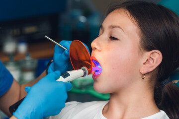 the dentist shines ultraviolet light on the child's filling.