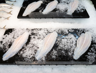 The white fish fillet on the black tray in the crushed ice for sale in the supermarket
