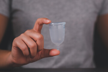 Hand holding menstrual cup. Studio picture of modern sanitary products for period. Women health, gynecology, hygiene, zero waste alternatives concept. Eco-friendly silicone menstrual cup for women.