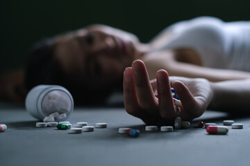 Cute woman wearing white tank top overdosed with pill bottles and pills on the floor.Selective focus on finger.