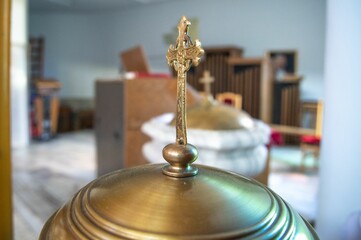 Selective focus shot of a gilded cross with blurred baptism attributes in the background
