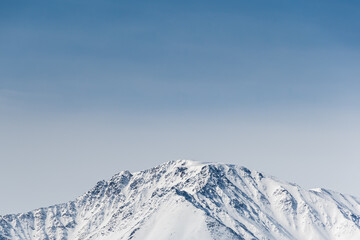 Snowy top of mountain range under blue sky