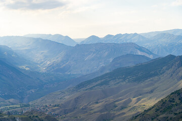 Naklejka premium Amazing landscape of mountain range with sunset sky and clouds and rural village in mountain valley in Dagestan. Scenery of mountain layer at dusk.