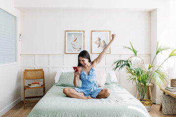 Happy young woman celebrating good news on mobile phone. Excited female cheering online success on...