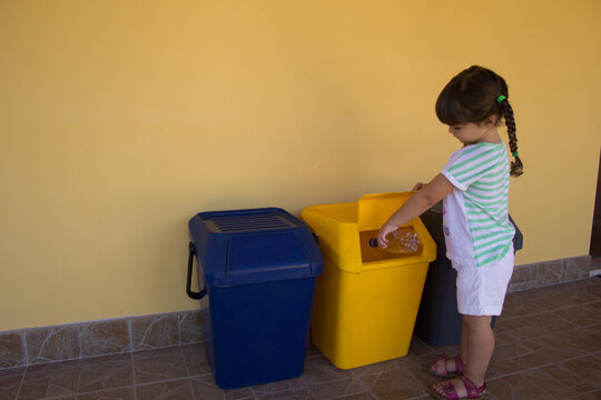 Image of an adorable little girl throwing a bottle of water into a garbage can. Reference to the education of children to respect nature and to recycle