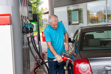 Mature man pouring petrol into tank of his vehicle on filling station. Travel,transportation and...