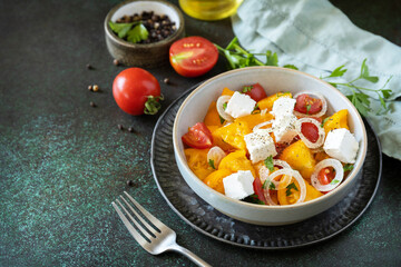 The concept of vegan or diet food. Tomato salad made from a mix of red and yellow tomatoes and feta cheese on a stone tabletop. Copy space.