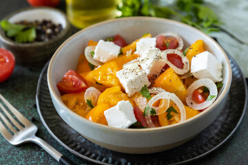 The concept of vegan or diet food. Tomato salad made from a mix of red and yellow tomatoes and feta cheese on a stone tabletop.