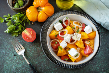 The concept of vegan or diet food. Tomato salad made from a mix of red and yellow tomatoes and feta cheese on a stone tabletop.