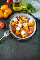 The concept of vegan or diet food. Tomato salad made from a mix of red and yellow tomatoes and feta cheese on a stone tabletop. Copy space.