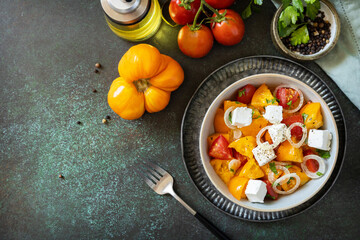 The concept of vegan or diet food. Tomato salad made from a mix of red and yellow tomatoes and feta cheese on a stone tabletop. View from above. Copy space.