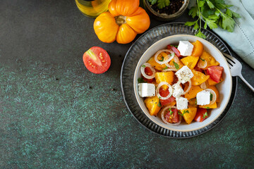 The concept of vegan or diet food. Tomato salad made from a mix of red and yellow tomatoes and feta cheese on a stone tabletop. View from above. Copy space.