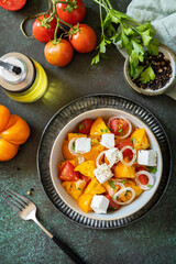 The concept of vegan or diet food. Tomato salad made from a mix of red and yellow tomatoes and feta cheese on a stone tabletop. View from above.