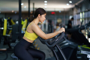 Beautiful Asian woman is working out in the gym by bike to get strong and beautiful muscled.