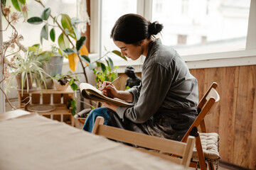 Young beautiful calm woman in grey shirt drawing in sketchbook