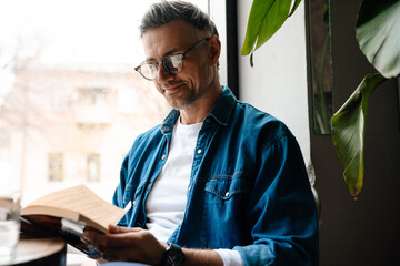 Adult handsome smiling man in glasses reading book - Powered by Adobe