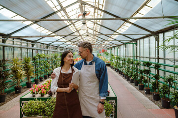 White happy man and woman standing by green plants while working in orangery