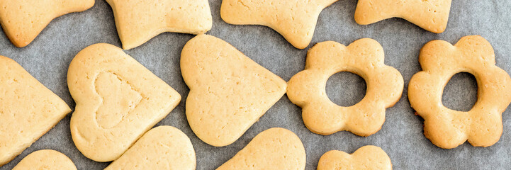 Baked shortbread heart and flower cookies on parchment paper banner. Wide panoramic header....