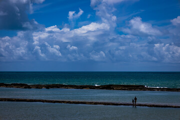 Fototapeta premium Silhouettes of a man and a child on a coral bar off the coast of Brazil. Human silhouettes