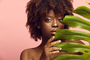 Curious black girl peeks out from behind monstera leaf. © Ilshat