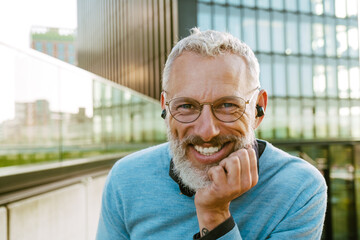 Mature grey man with beard laughing and listening music at city street