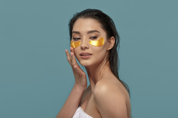 Beautiful happy lady using eye patches mask on blue.