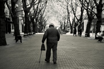 Grayscale of an old man with a stick walking in a park