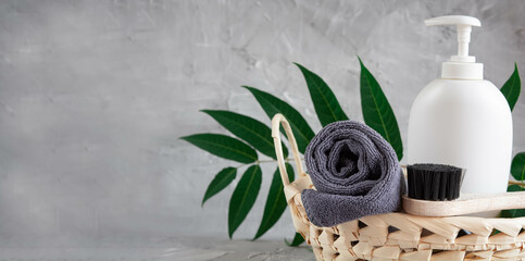 Gray towel, body massage brush, black bristle brush, foot penza, green ailanthus branch on gray background, bath accessories concept, bath products - obrazy, fototapety, plakaty