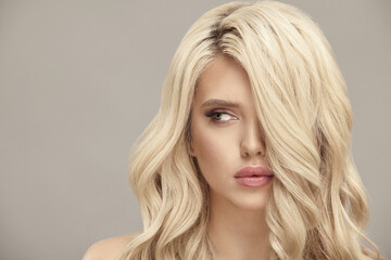 Naklejka premium Blonde woman with long wavy hair looks aside on beige isolated background with free copy space.