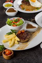 Grilled beef steaks with potato, vegie and steak sauce at white plate on texture rustic table