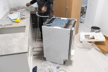 Appliance technician working under a kitchen sink installing a dishwasher