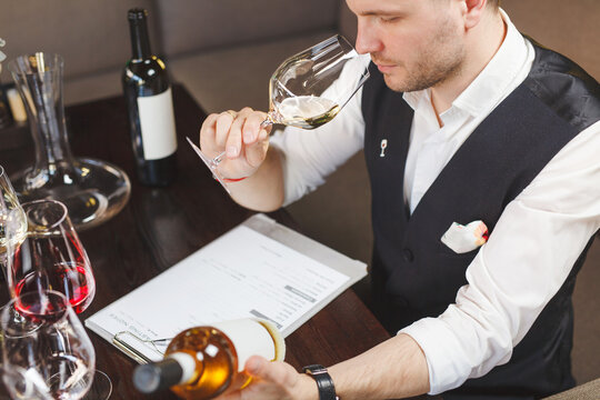 Wine waiter smells white drink in wineglass in winehouse.